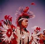 Kainai First Nation (Blood Tribe) man wearing a headdress and beaded clothing for the Sun Dance ceremony, Alberta. 1960