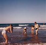 [A man taking a photograph of a man, a woman and a child in the water, Prince Edward Island] 1956