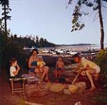 [Family enjoying a meal at the beach, seated around a fire, British Columbia] 1956