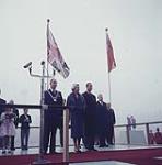 H.M. Queen Elizabeth II and H.R.H. Prince Philip bring greetings to 15,000 school children, assembled on the grandstand at Lansdowne Park, Ottawa, Oct. 16, 1957. In their company are Prime Minister John Diefenbaker, Mayor George Nelms is seen on H.M.'s right. To the right are the representatives of the school children, who presented a nosegay to the Queen, namely Gail Cook and Robert Allard. October 16, 1957.