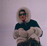 A woman wearing a parka and a pair of sunglasses. Frobisher Bay, Northwest Territories May 1958.