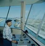 The operator of the lower control tower of the Upper Beauharnois Lock, P.Q. In the background, a vessel having transited the lower Beauharbius Lock (about 3/4 miles of a mile downstream), is approaching the Upper Lock. The minimum width of the channel between the two locks is 200'. The depth is 27' mai 1959