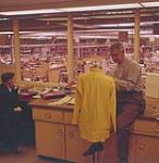 A man measuring blouse on dress form in office of Gerhard Kennedy clothing factory. Winnipeg, Manitoba.  [Homme mesurant une blouse sur un mannequin dans le bureau de la fabrique de vêtements Gerhard Kennedy. Winnipeg, Manitoba] mars 1960