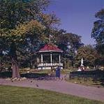 A young lady feeding the pigeons in front of the little band stand which is in the Halifax public gardens. Halifax, N.S.  1961