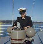 Ship captain examining equipment on ship's deck. février 1961