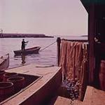 A boy standing in rowboat holding a paddle, Prince Edward Island. 1961