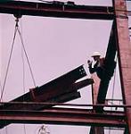 [Construction worker standing on metal beam directing the lowering of metal beams during construction of the Teron Building, Ottawa, Ontario.] May 1961.