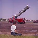 A young boy, sitting down, looking at a new aerial ladder being tested. Charlottetown, P.E.I.  1961