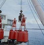 Hooking onto a buoy to drop it over the side. Seaway Spruceup. mars 1961