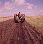 Four men sitting on the tractor preparing crops in field. Ardath, Saskatchewan. 1961