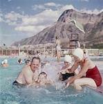 Jimmy Gault receiving his first swimming lesson at Waterton Lakes National Park swimming pool, Alberta. Vimy Ridge can be seen in the background.  août 1961