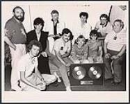The Cars receive Double Platinum for "Heartbeat City" while in Toronto for their concert at the CNE Grandstand. Pictured from left are: Larry Green, Kim Cooke (WEA), Ric Ocasek, Ben Orr (Cars), Randy Sharrard (Wea), David Robinson (standing), Greg Hawkes, Elliot Easton (Cars), Garry Newman and Roger Desjardin (WEA) [entre 1984-1985].