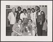 Motown recording artists The Commodores being presented gold albums and a gold single for their album and song "Nightshift" at a private party at the Roots department store in Toronto. Back row, left to right: George Struth (President Quality Records), Ronald LaPread, Walter "Clyde" Orange, J.D. Nicholas, William King (The Commodores), Frankie Gaye. Front row: Cameron Carpenter (Motown Label Mana [entre 1985-1990]