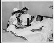 A team of health care professionals tend to a patient in bed. L to R: Certified Nursing Aide, Professional Student Nurse, a Doctor, and a Registered Nurse. Edmonton. Nurses and Nursing. Department of Citizenship and Immigration, Information Division [between 1930-1960]