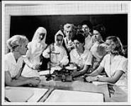 Sister Ste. Croix, professor of nutritive chemistry, is explaining the stability of whipped egg whites in non-fat cakes to a group of graduating students in the Faculty of Art's School of Home Economics. Ottawa (?). Occupations - Professional chemists. Department of Citizenship and Immigration, Information Division [entre 1930-1960]