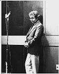 Portrait of Keith James leaning against the wall by a microphone on a floor stand [between 1975-1985]
