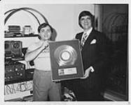 Portrait of Barry Stafford (Quality Records) and music producer Robert Ouimet holding Ouimet's award for the disco song Keep On Jumpin 1978