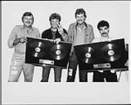 "Backstage following their recent sold-out performance at the new Kingswood Theatre at Canada's Wonderland, RCA's Mike Gaitt and Ken Bain presented Hall & Oates with double platinum for their hit album H2O. RCA's Ken Bain holds up three fingers signifying H2O had attained triple platinum in Canada the day of their concert." ca. 1982.