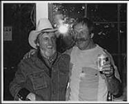 Two unidentified smiling musicians, one wearing a cowboy hat, one holding a can of beer [entre 1985-1995].