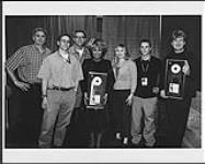 Tina Turner holding an album award, posing with five unidentified men and one woman 2000