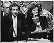 Tim Taylor speaking into a microphone at a podium, and standing next to Anita Perras who is holding an award [entre 1984-1987].