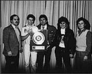 Holly Woods and Scott Kreyer of "Holly Woods and Toronto" present the students of Dr. Norman Bethune Collegiate Institute with a gold record for their support of the benefit concert 'Sounds United '83'. (l to r) David Mervold (Dr. Norman Bethune Collegiate Institute), David Anderson (student council president), Scott Kreyer, Holly Woods, Donna Taggart (United Way) 1984