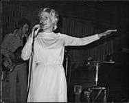 Lynn Jones singing into a microphone on a stage s.d.