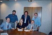 Snapshot of Mae Moore signing with EMS. Also pictured are Rick Camilleri (?) and four unidentified men [between 1990-2000]