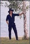 John McCabe standing next to a birch tree in front of a lake [between 1970-1975].