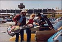 Dieter Boehme, Peggy Burns et Dick Damron tentant d'entrer des valises dans une Mustang 1966 à l'aéroport de Vancouver lors de leur arrivée pour la Semaine de la musique country, 9 septembre 1987 9 septembre 1987