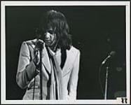 Eddie Money standing at a microphone [between 1977-1980].