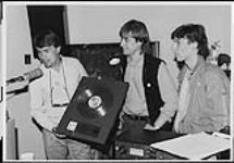 Attic Records presents CFNY-FM with gold Nylons LP to commemorate gold sales for "Seamless", the third Nylons LP and also the group's first-ever live broadcast. Pictured left to right are Lindsay Gillespie (Attic Marketing), Ralph Alfonso (Attic National Promotion), and Eddy Valiquette (M.D.) [ca 1984].