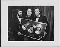 Willie Nelson accepting triple platinum for his album "Stardust". Pictured left to right are Al Teller (Senior Vice President and General Manager, Columbia Records), Willie Nelson, Rick Blackburn (Senior Vice President and General Manager, CBS Records Nashville) [entre 1983-1984]