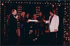 Four rock and roll impersonators holding a cake for Bobby Curtola [entre 1988-1995].