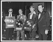 Buck Owens' Manager, Jack McFadden, Maurice Zurba of Capitol Records, Recording artist, Buck Owens and Ed LaBuick, President of TeeVee International, receiving Gold awards for the TeeVee album "Buck Owens - 20 Greatest Hits" [between 1977-1978].