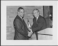 Gerry LaCoursiere and Peter Steinmetz, hold a Juno Award while shaking hands [entre 1980-1990].