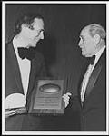 An unidentified man holds the Wm. Harold Moon Award, the award was given to Frank Mills and presented by Harold Moon [ca. 1980].