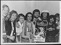 Group of people posing with a 'Sold-Out' award for a Trooper concert, presented to Jack Skelly, Winnipeg - (left to right) Frank Ludwig, Doni Underhill, Valerie Skelly, Ra McGuire, Jack Skelly (Sales/Promotion Manager of MCA Records), Brian Smith, Miles Cohen, Tommy Stewart [entre 1975-1980].