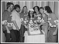 Trooper coupant un gâteau lors d'une conférence de presse à Winnipeg, (de gauche à droite) Bruce Wall, Jack Skelly, Frank Ludwig, Tommy Stewart, Brian Smith, Doni Underhill, Ra McGuire [between 1975-1980].