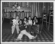 Trooper prenant une pose à côté d'un prix d'album et d'une affiche du logo de leur groupe [ca. 1978].