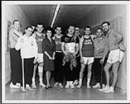 Brian Skinner and an unidentified group of men dressed in sports gear, standing with Annette Funicello [entre 1969-1972].