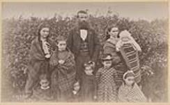 Portrait of a man and a woman with seven children and an infant standing in front of a bush, Osnaburgh House, Ontario 1886.