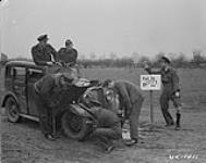 Equipped with their own cars, some flyers in RCAF Bomber Group often enjoy rides around the country. Standing with the shot-gun, the owner of the car, F/L Raymond Beauchamp on his right, F/O G. Wild of the RAF. F/L E. St-Jean, DFC is trying to pump a tire while F/O N. Lejambe is removing the jack. On his right, F/L R. St-Armour, S/L R.D. Hemphill, DFC at the extreme right. 425 Squadron 21 February 1945.