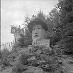 Large wooden sign in the shape of a head warning drivers to be cautious, on the Trans-Canada Highway between Golden and Revelstoke, British Columbia 17 août 1954.