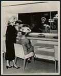 [Two women trying on hats, Regina, Saskatchewan, 1950s] ca. 1950