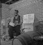 E.H. House avec une boîte de cyanure gazeux utilisé pour désinfecter les articles contaminés dans l'installation de fumigation du poste de quarantaine de Santé nationale et Bien-être social juin 1948