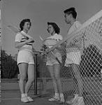 Rose Young, Beverly Chan, and Dexter Fong, gather in front of a tennis net 1951