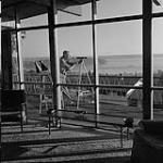 Len Norris looking through a telescope in his home 1958