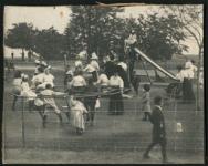 "Children playing on merry-go-round and slide with adults visiting" vers 1910.