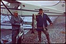 [Men holding arctic char by a seaplane] [between 1900-1976]